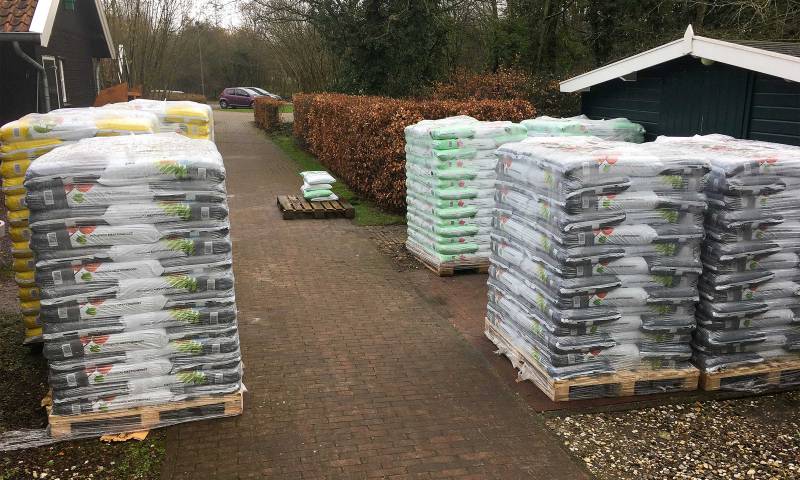 Pallets met hoogopgestapelde zakken potgrond voor de deur van de winkel